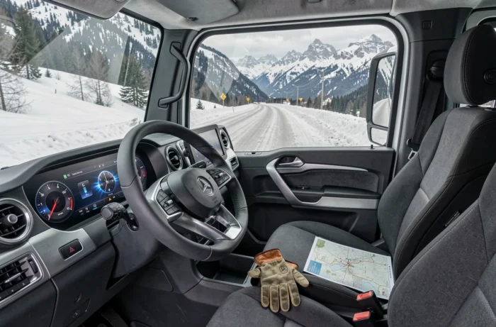 Intérieur modernisé du Mercedes Unimog 2025 avec tableau de bord numérique et vue sur route alpine enneigée
